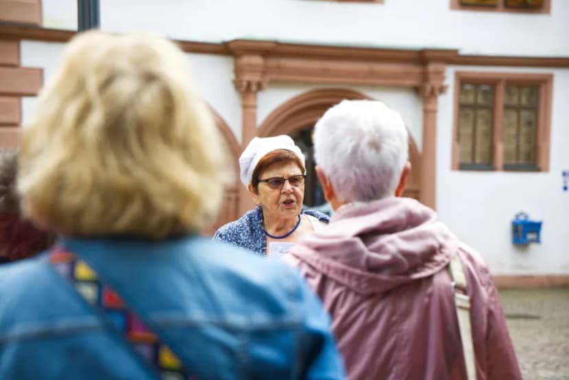 Eine Kostümführerin führt als Wirtin eine Gruppe von Menschen durch die Innenstadt. Im Hintergrund ist das Alte Rathaus in Lohr am Main zu sehen. Vor der Kostümführerin stehen zwei Frauen, die von hinten zu sehen sind.