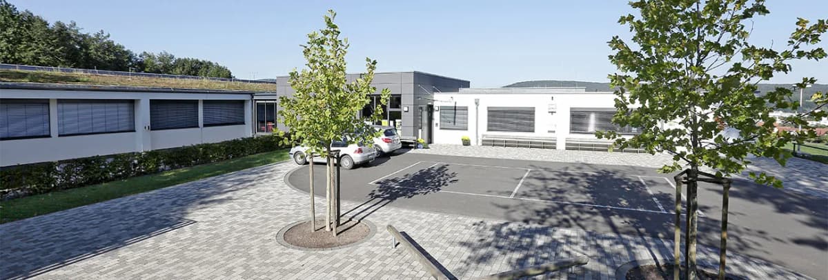 Flachdachgebäude mit Parkplatz und begrüntem Dach, umgeben von Bäumen