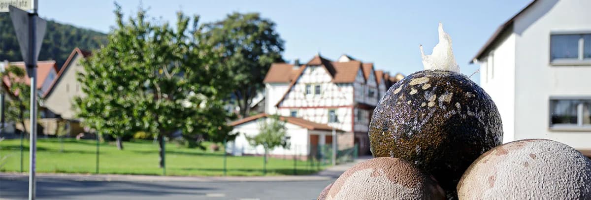Kugelbrunnen im Vordergrund, im Hintergrund Fachwerkhäuser und Straße im Ortsteil Wombach