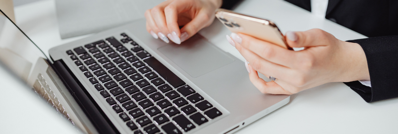 Hände an einem Notebook, eine Hand hält zusaätzlich ein Smartphone